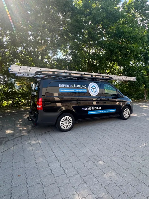 Einsatzfahrzeug von ExpertRäumung: schwarzer Transporter mit der Beschriftung „ExpertRäumung", darunter „Haushaltsauflösung · Entrümpelungen", und Leiter auf dem Dachträger