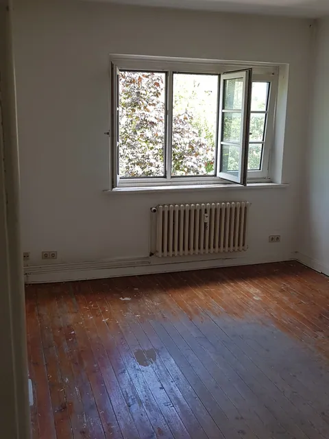 Leeres Zimmer nach einer Wohnungsauflösung: Dielenboden, Heizkörper unter dem Fenster, keine Möbel mehr